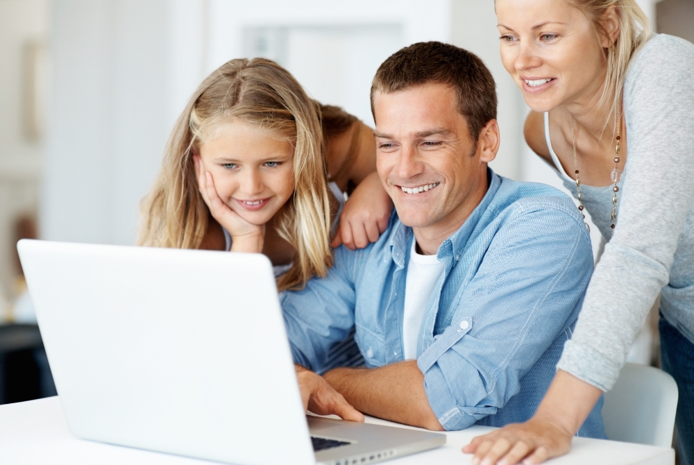 family gathered at kitchen table looking at laptop screen